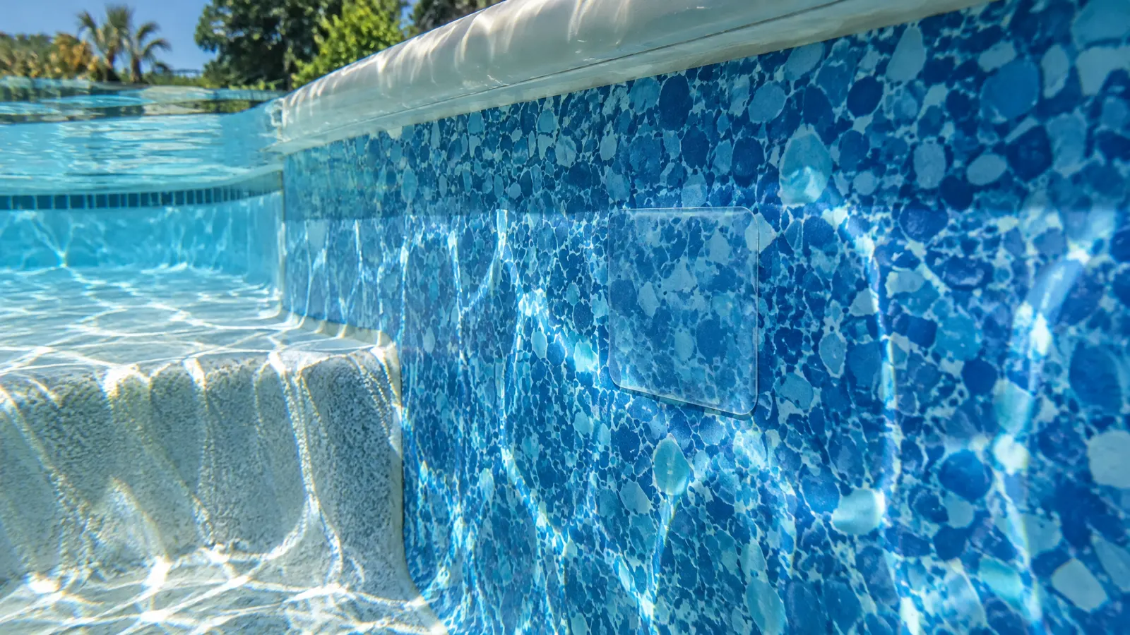 Vinyl pool liner wall underwater with a neat patch repair beside a pool step